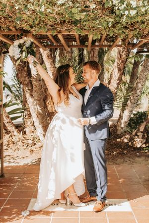 Wedding couple dancing and twirling under a vine-covered outdoor pergola.