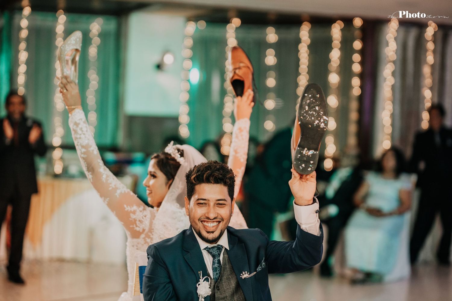 A joyful celebration moment at a wedding reception with raised arms and string lights in the background.