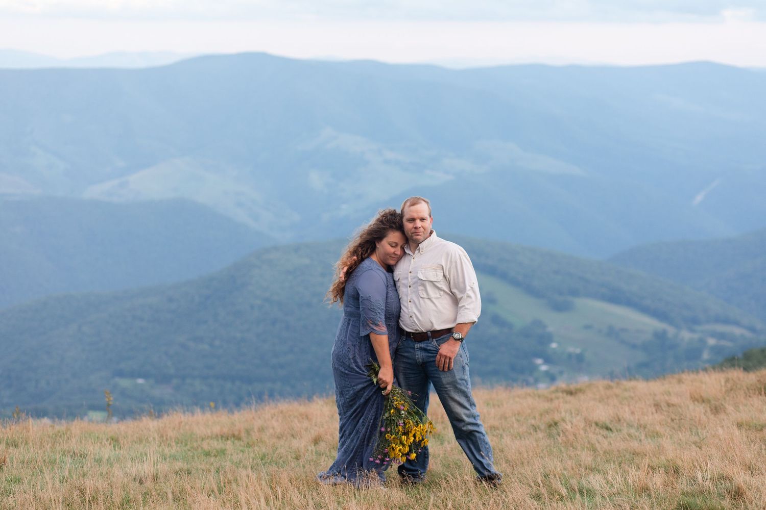 Scenic mountain landscape with couple sitting on rocks in golden meadow.