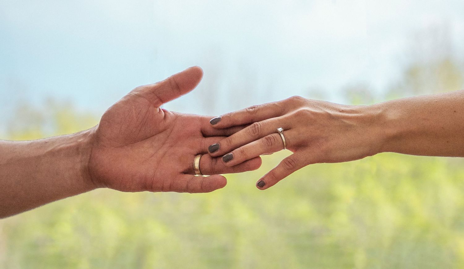 2 hands reaching out for each other just touching fingers, showing off their wedding rings while looking ever so effortless