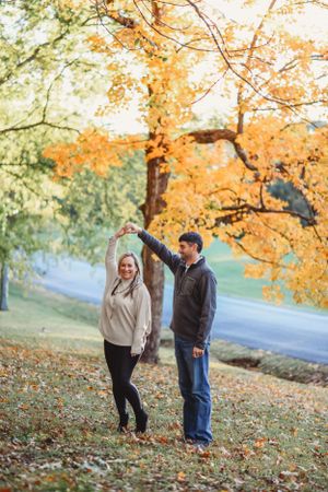 A couple enjoys a romantic autumn moment under golden maple trees on a winding path.