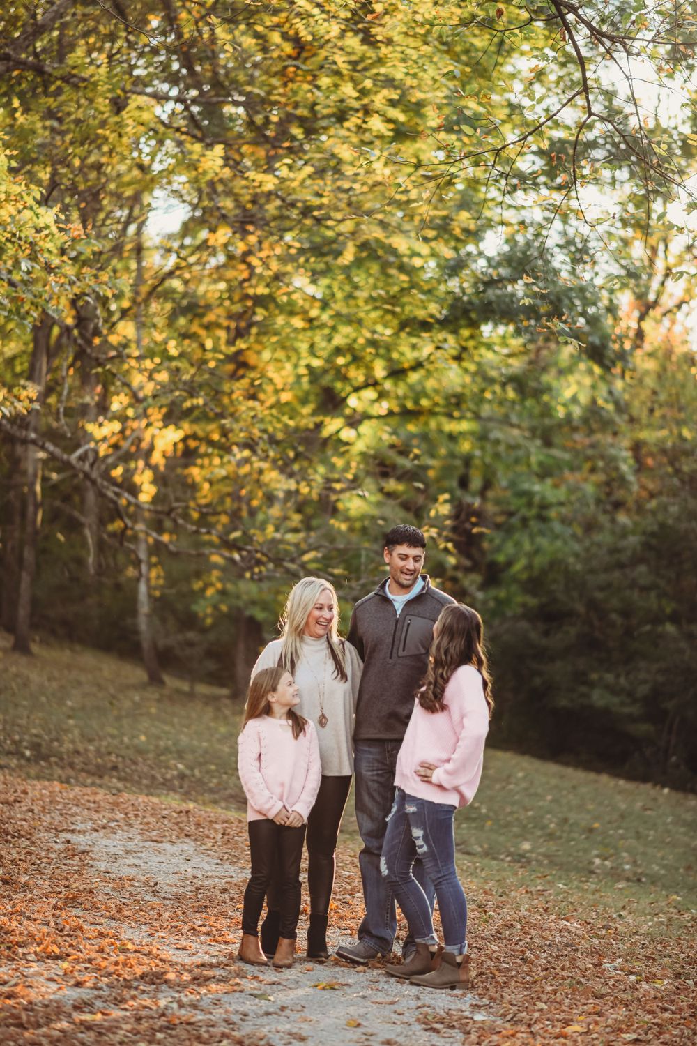Family walking together on an autumn path with golden leaves and trees in the background.