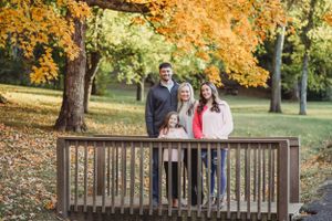 Family portraits on a wooden bridge surrounded by vibrant fall foliage.