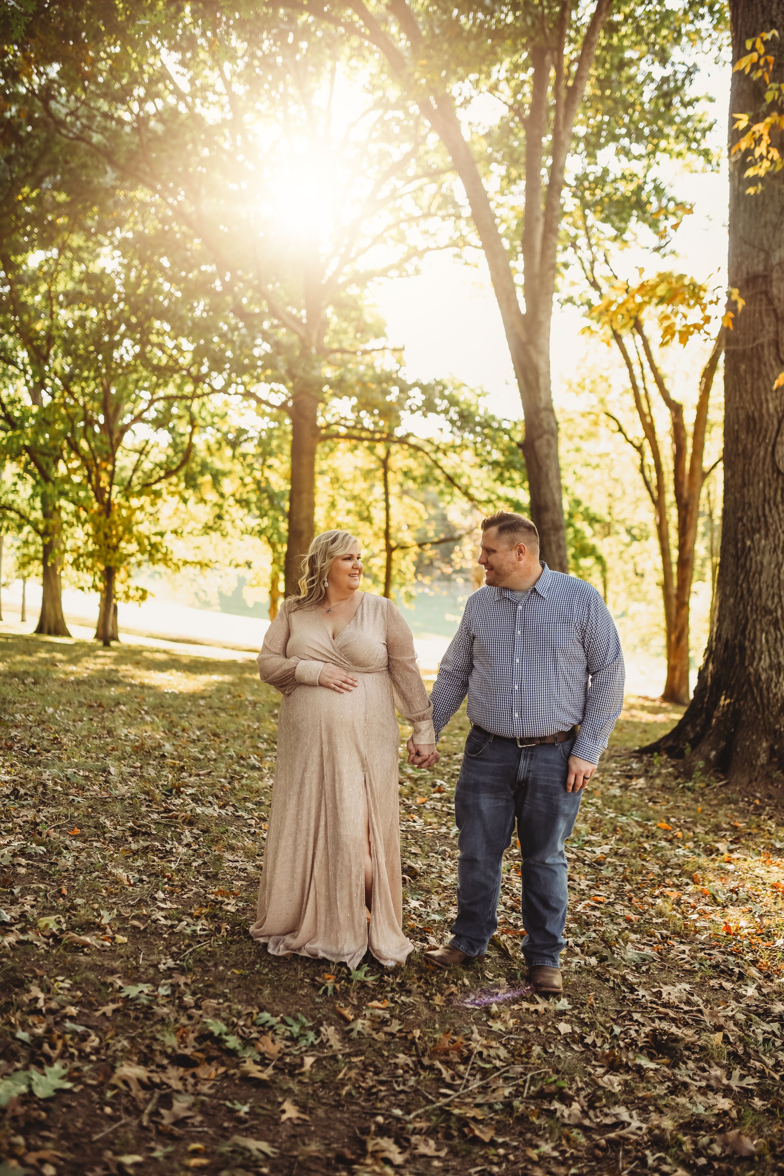 A couple takes romantic photos in formal wear among fall trees at sunset.