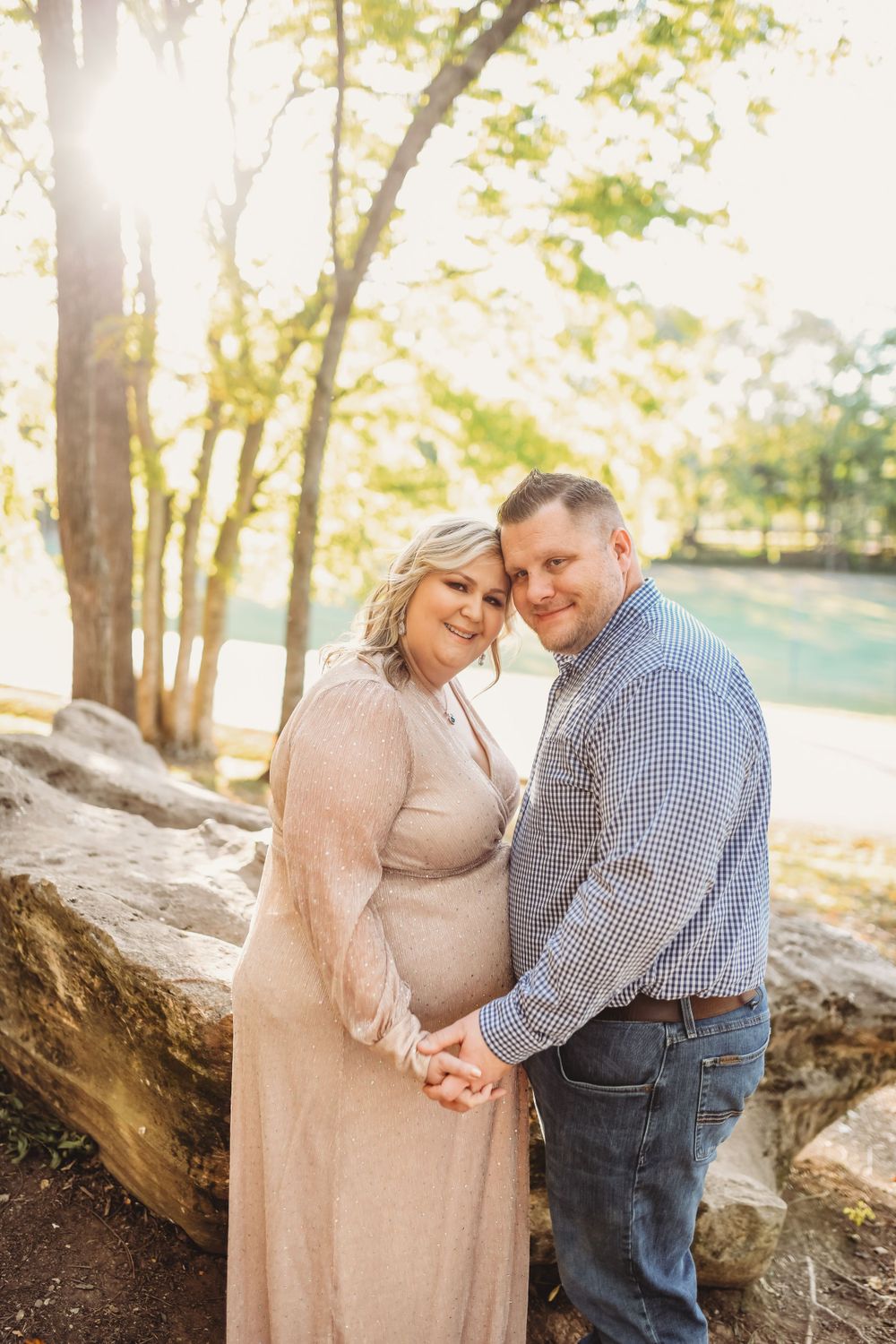 A couple shares an intimate moment during their maternity photoshoot in a natural setting.
