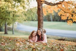 Two people lying in colorful fall leaves during an outdoor photo session.