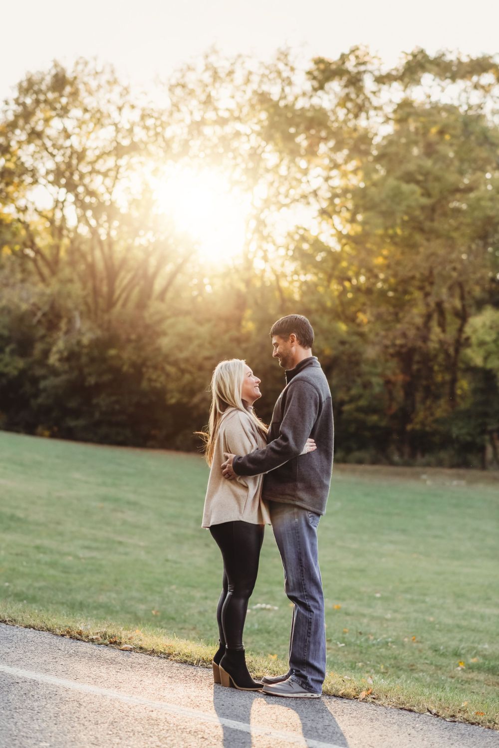 A couple embraces on a path at sunset with golden sunlight streaming through autumn trees.