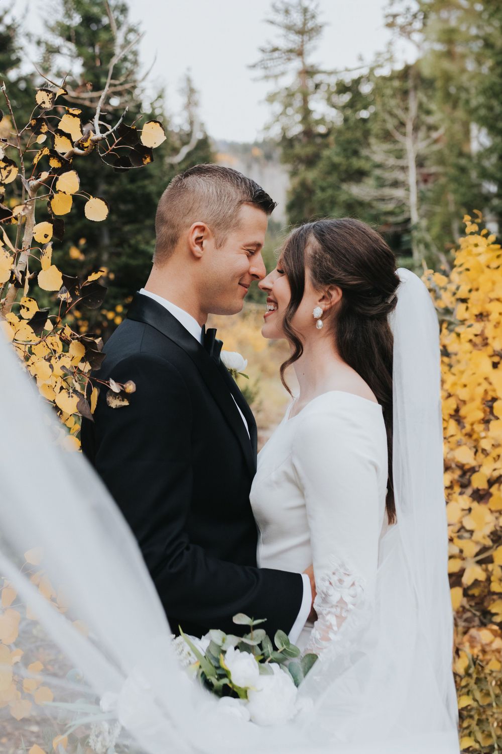 A bride and groom smile amidst the fall foliage near Solitude, Utah. Captured by Utah wedding photographer, Katie Griff