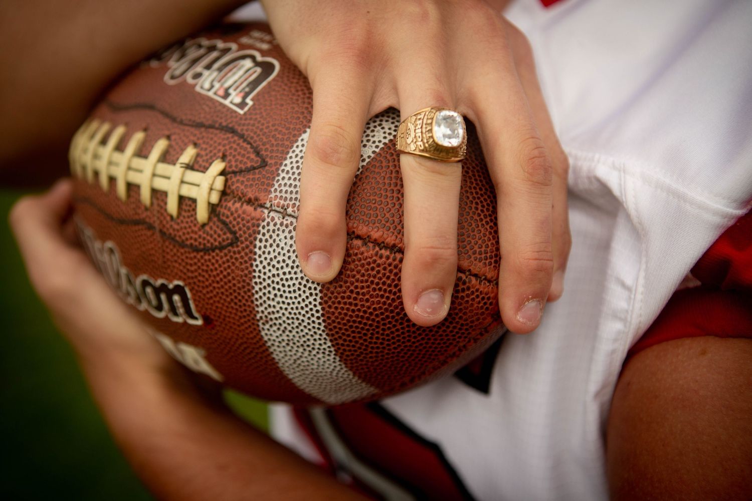 Close-up of hands holding a football while wearing a championship ring.