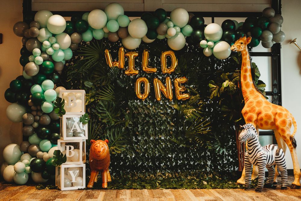 Safari-themed birthday party setup with 'WILD ONE' balloon letters, green balloon arch, and decorative giraffe and lion.