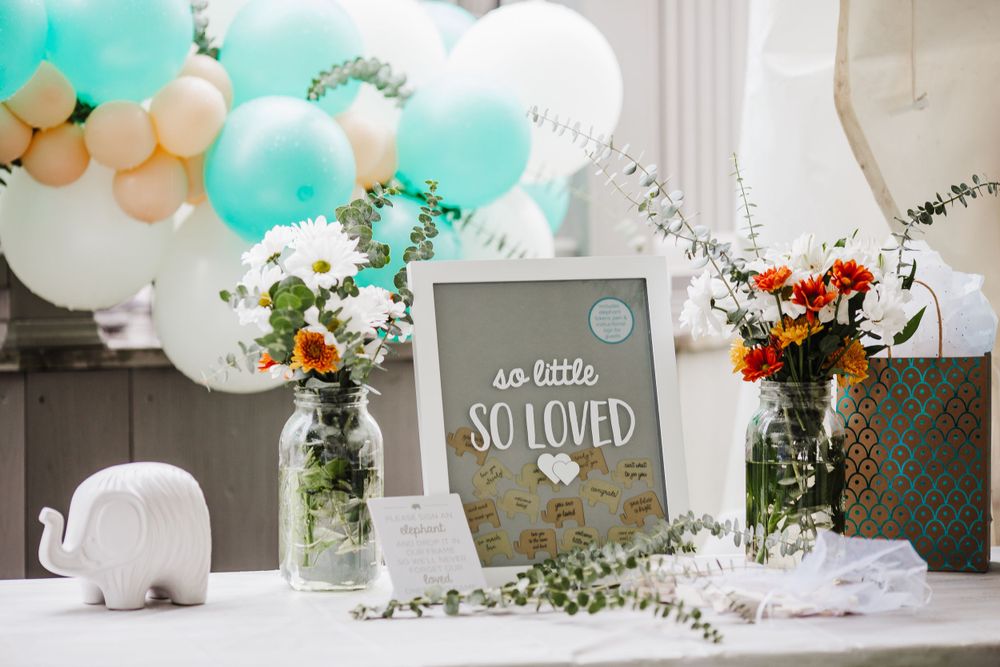 Baby shower decorations with teal and white balloons, flowers, and a framed sign.