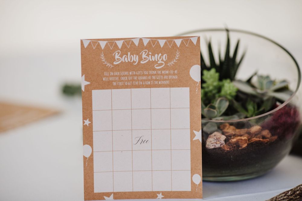 A kraft paper baby shower game calendar sits next to a small succulent terrarium.