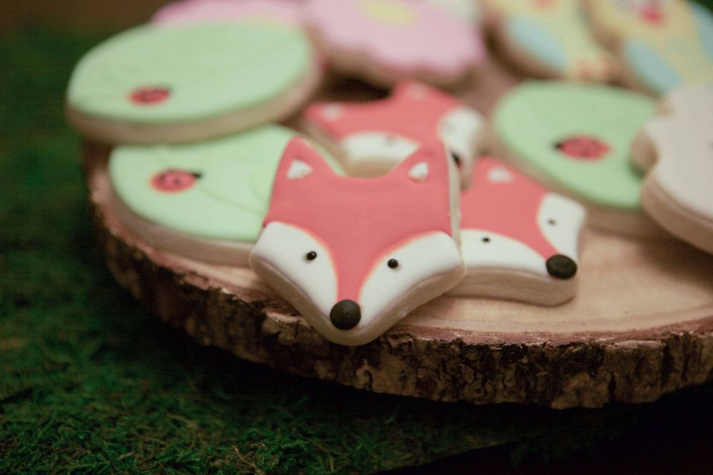 Cute fox-shaped sugar cookies decorated in mint green and coral pink on wooden slice.