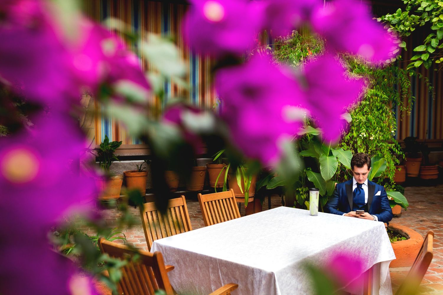 A table with white tablecloth outdoors framed by vibrant pink flowers in the foreground.