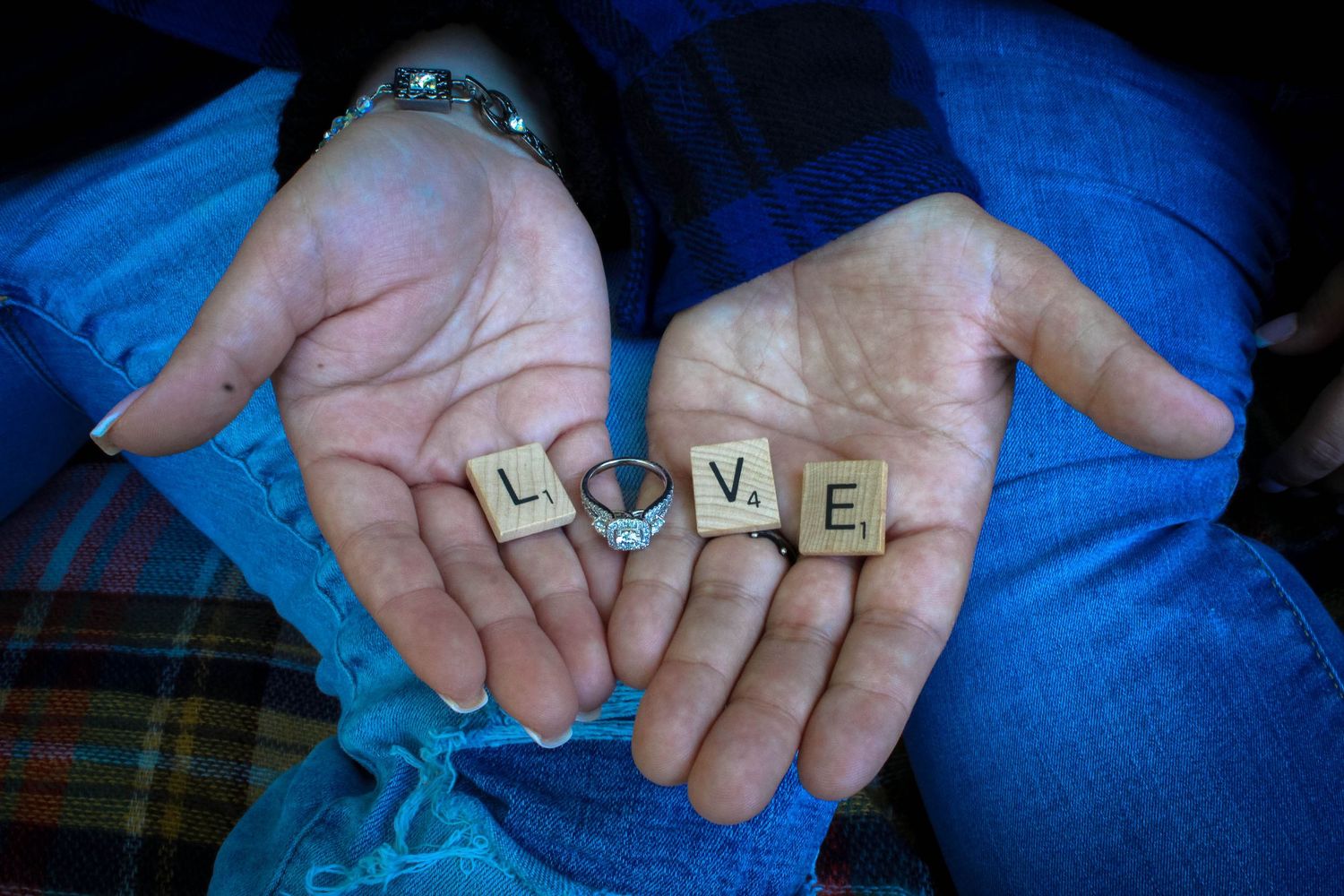 Open hands holding wooden letter tiles spelling out LOVE against blue denim.