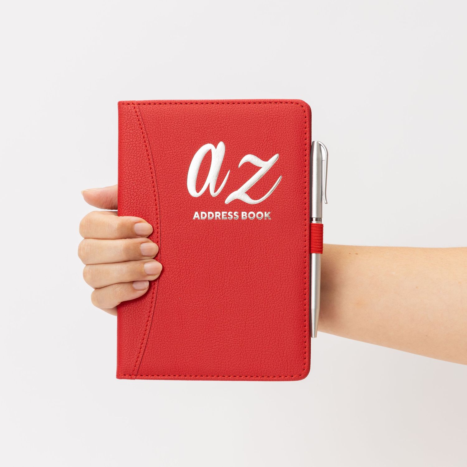 Hand holding a red leather A-Z address book with pen on white background.