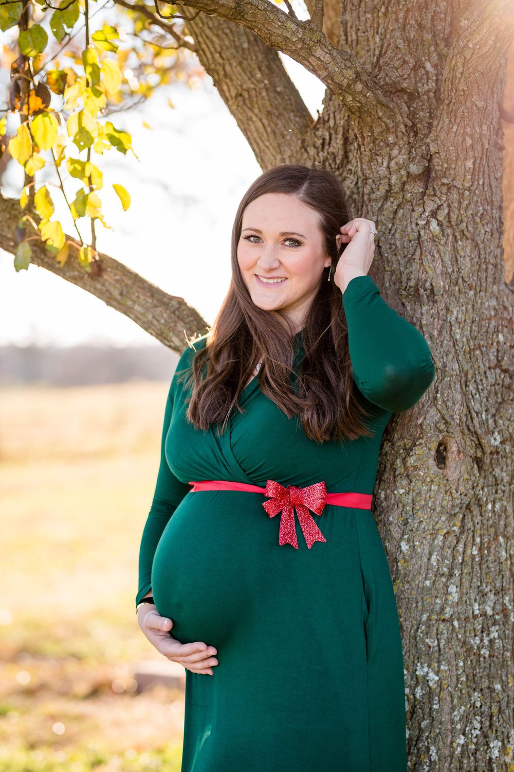 Expectant mother in a green dress by a tree during an outdoor maternity session in West Plains, Missouri