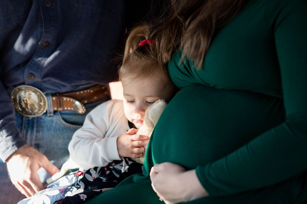 Toddler leaning against her mother's belly during an outdoor maternity session in West Plains, Missouri