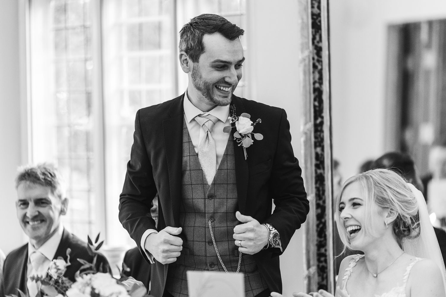 A black and white photo captures joyful laughter during a wedding reception speech.