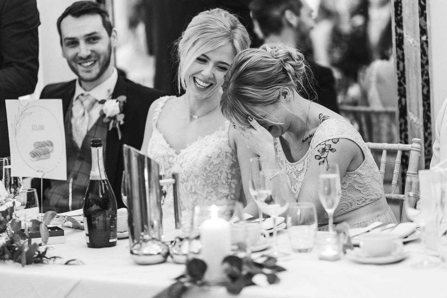 Wedding reception guests share an emotional moment of laughter at an elegant table setting.