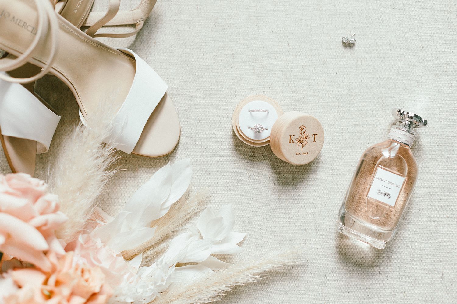 Wedding accessories flat lay with perfume bottle, shoes, and delicate dried flowers in neutral tones.