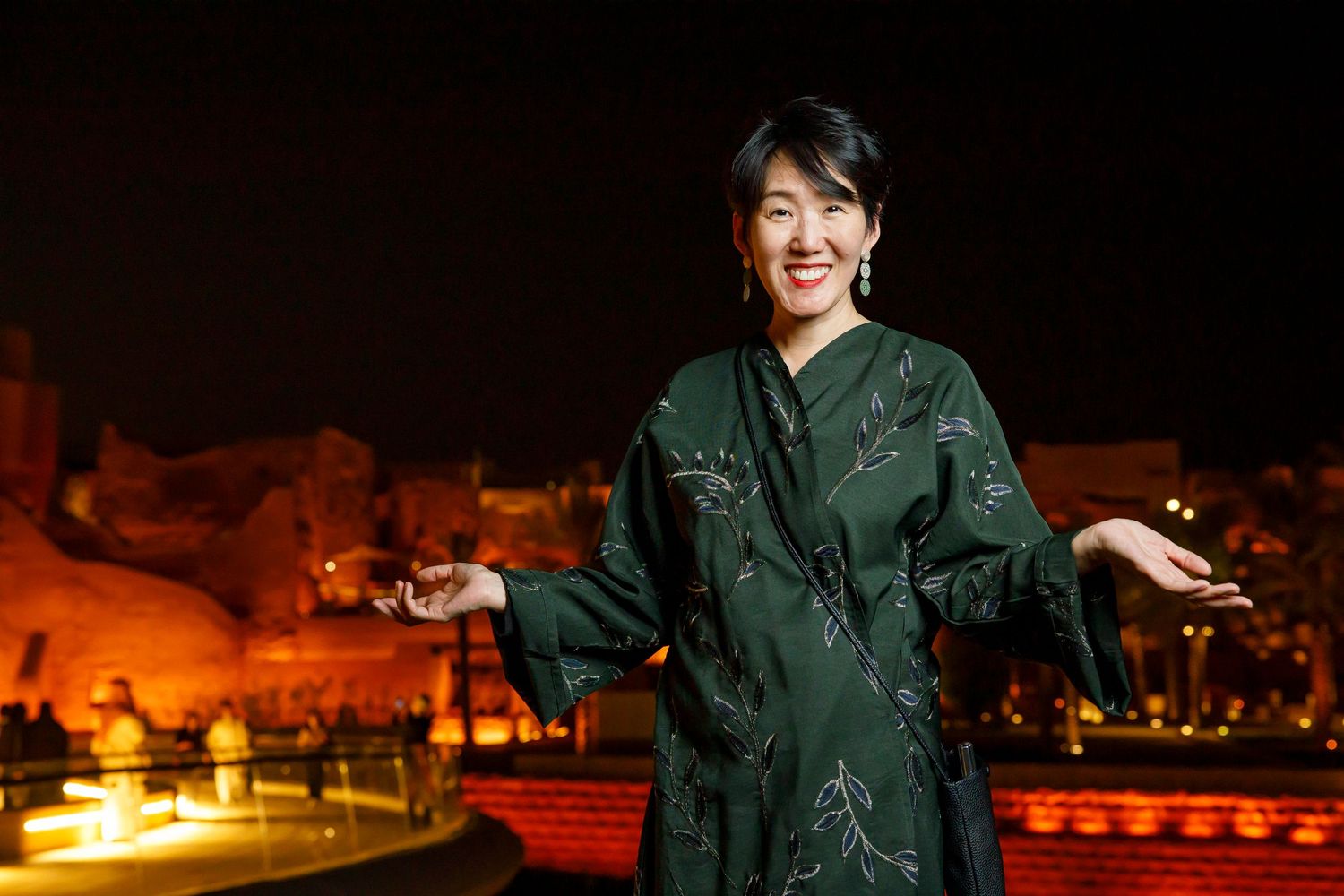 Person in green outfit smiling at night with warm desert backdrop.
