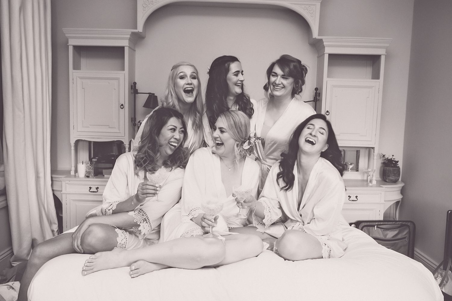 Bridal party shares joyful moment together on bed during wedding preparations.
