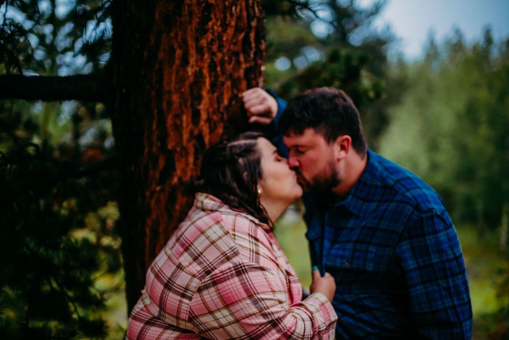 Intimate couple's portrait among pine trees in casual flannel shirts.