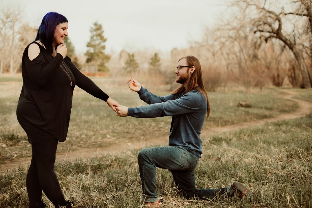 Romantic proposal scene on dried grass with autumn trees in the background.