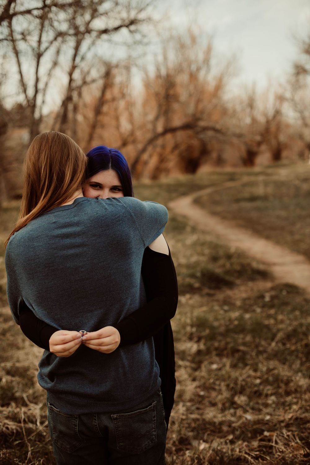 Intimate embrace captured on an autumn path with bare trees in the background.