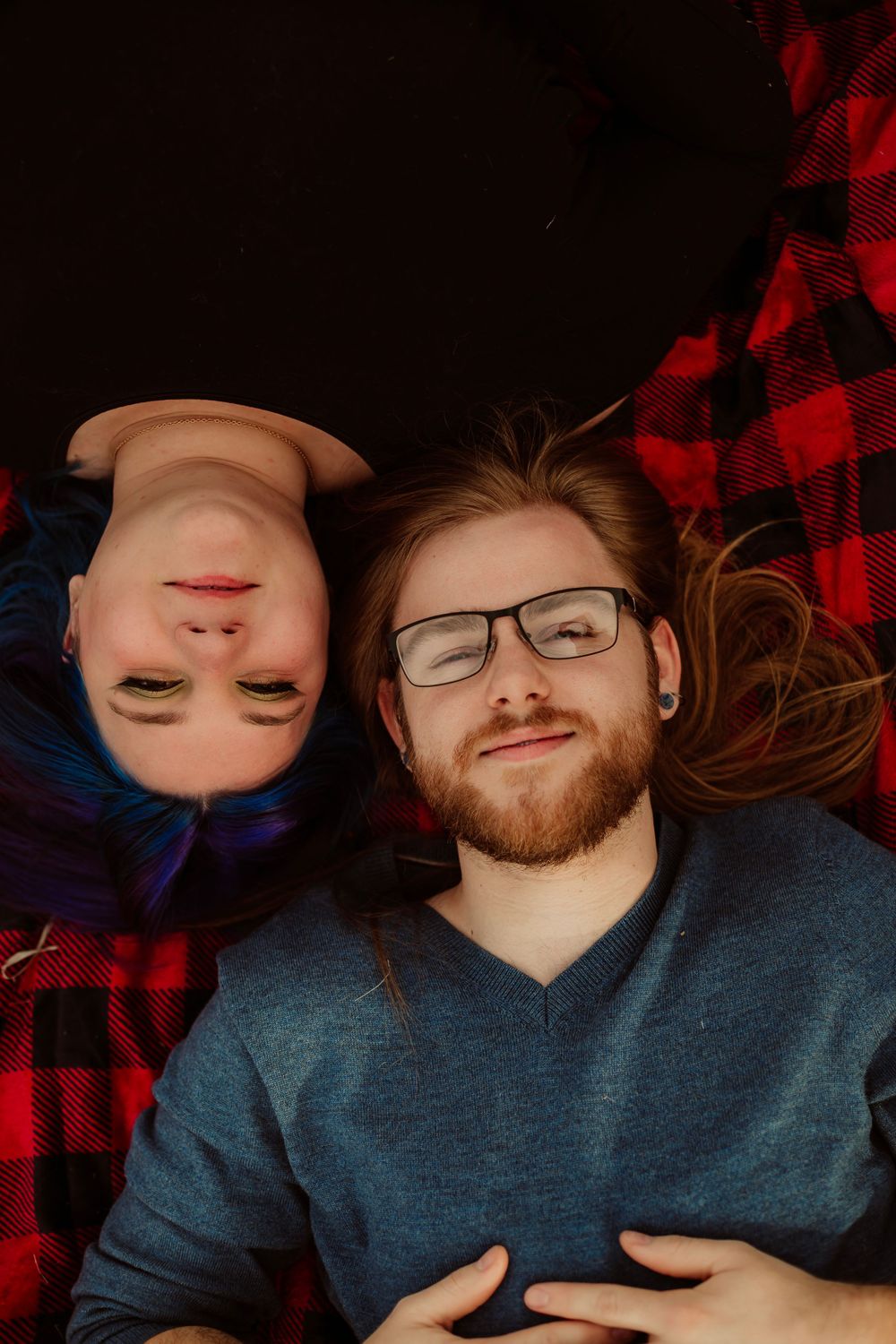 Couple lying on red plaid blanket with creative upside-down composition.