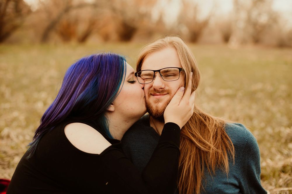 Intimate couple portrait in autumn field with blue-haired woman and long-haired partner.