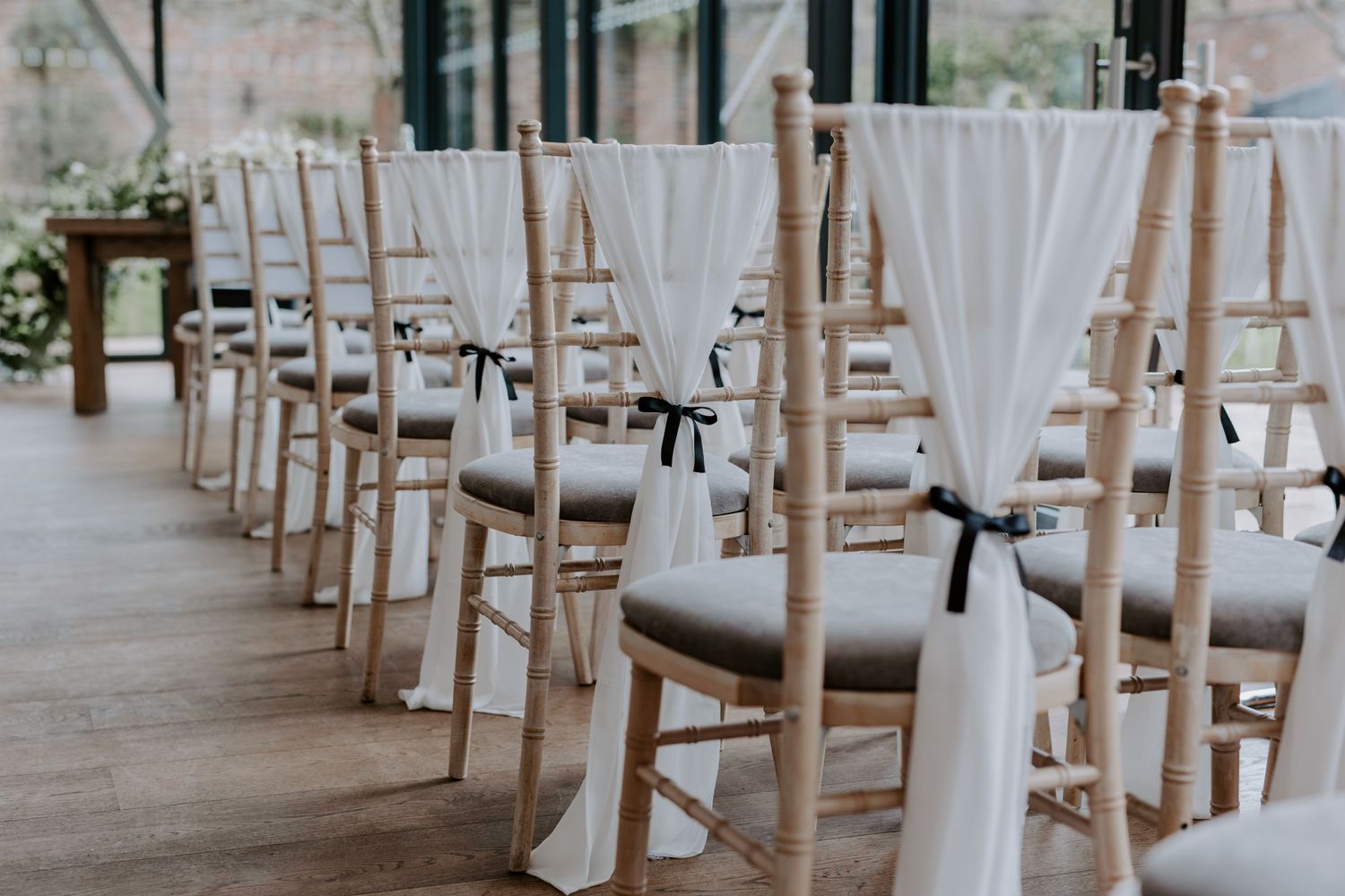 Cream chairs with white draping on the back with simple black bows.