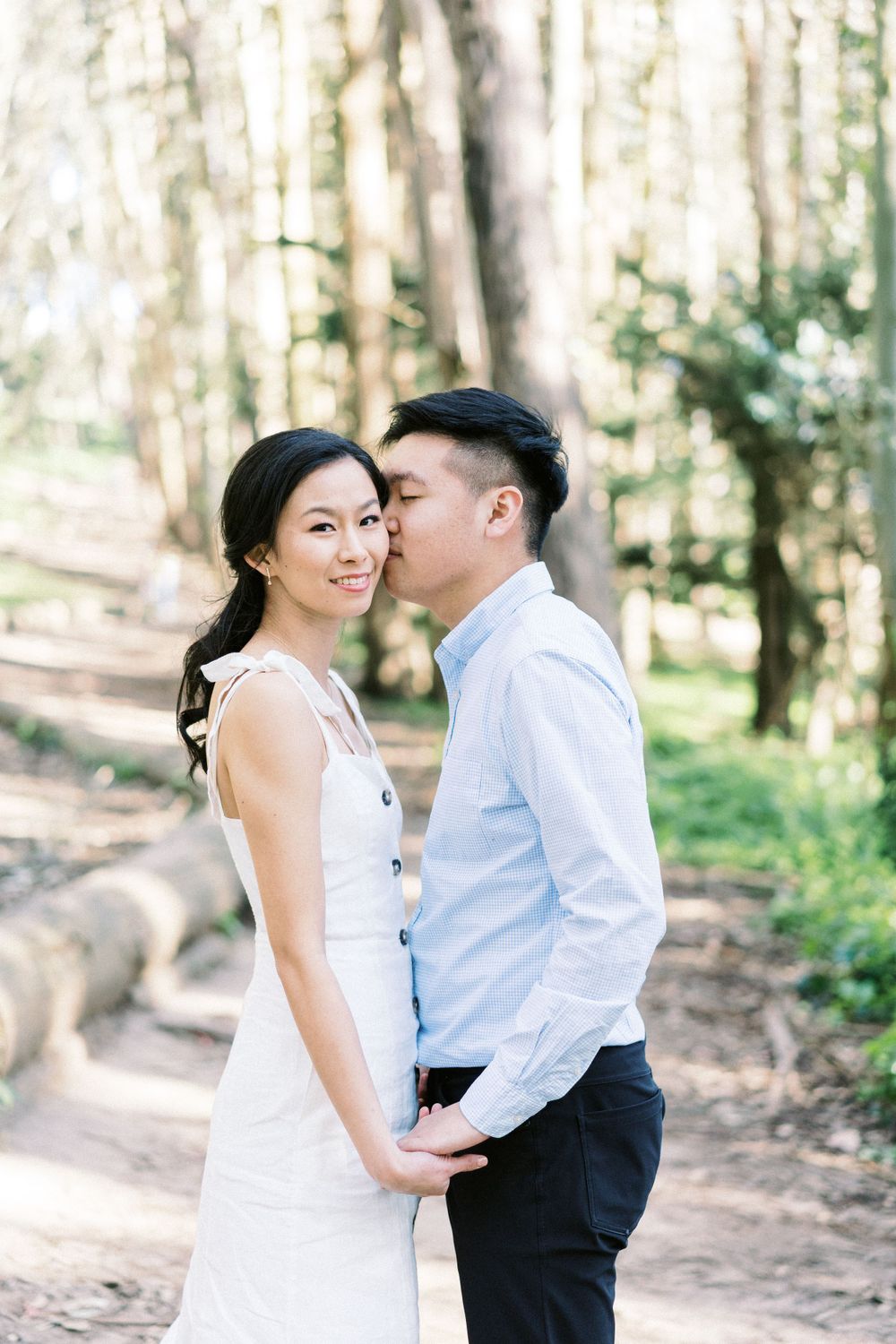 An intimate moment between a couple on a scenic forest trail surrounded by tall trees.
