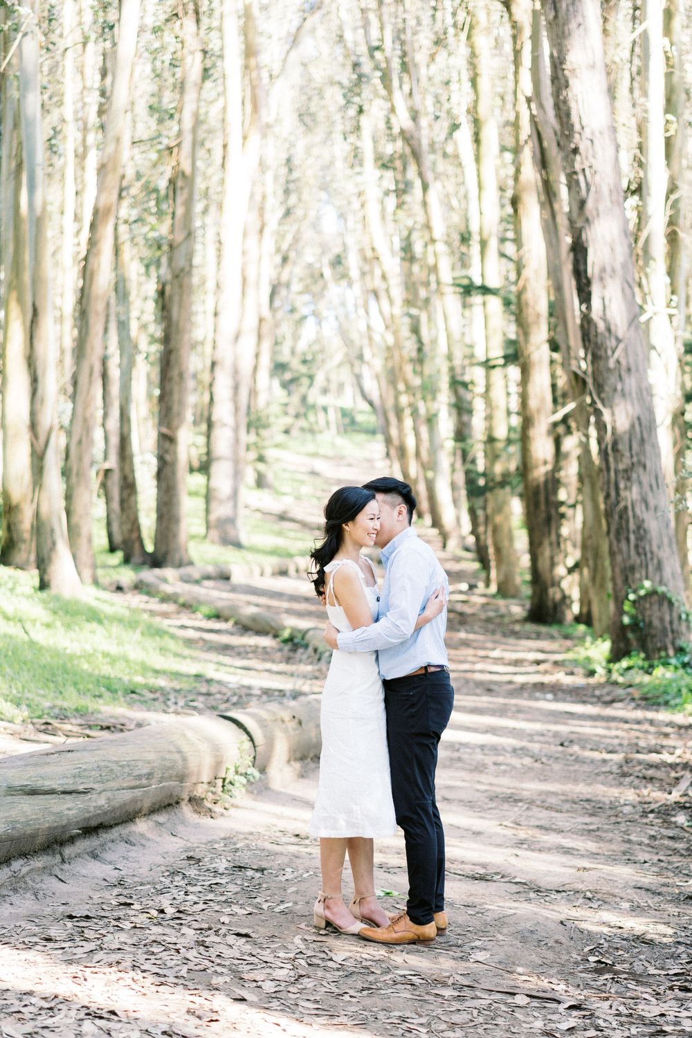 A couple shares a tender moment on a forest trail surrounded by tall eucalyptus trees.