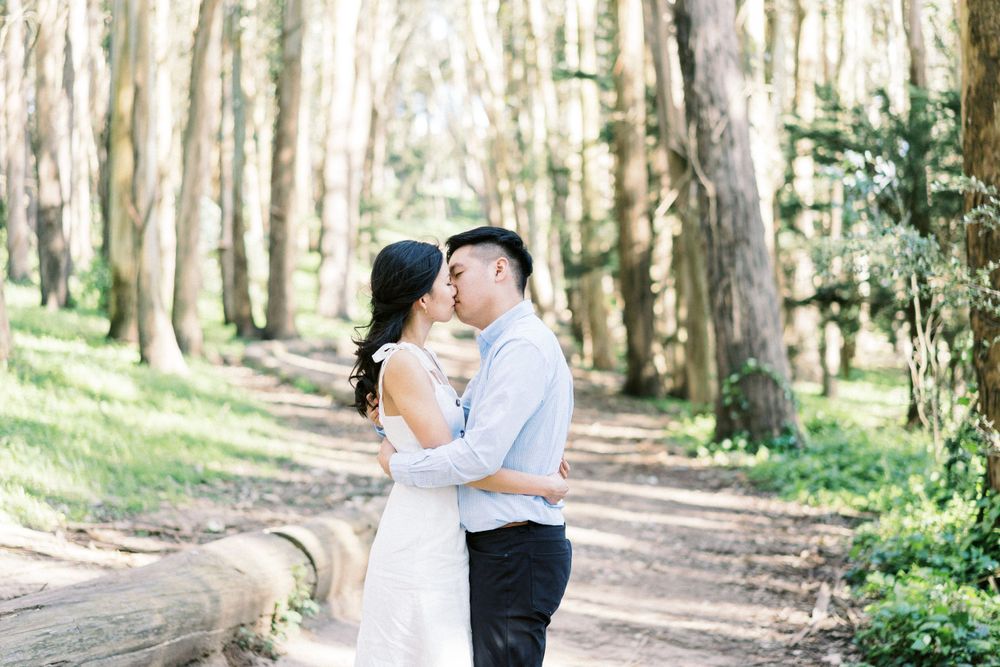 A romantic embrace between a couple on a tree-lined forest path.