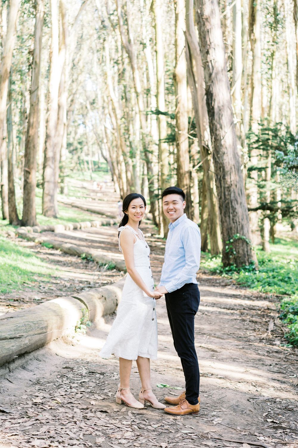 A couple poses together on a winding forest path among tall eucalyptus trees.