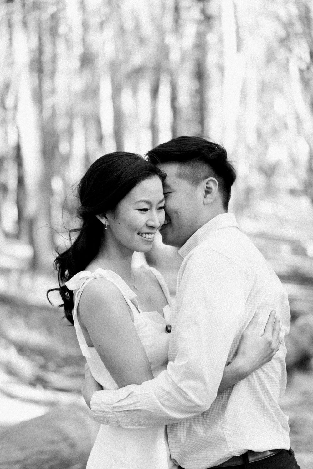 A black and white portrait of a couple sharing an intimate moment in a forest setting.