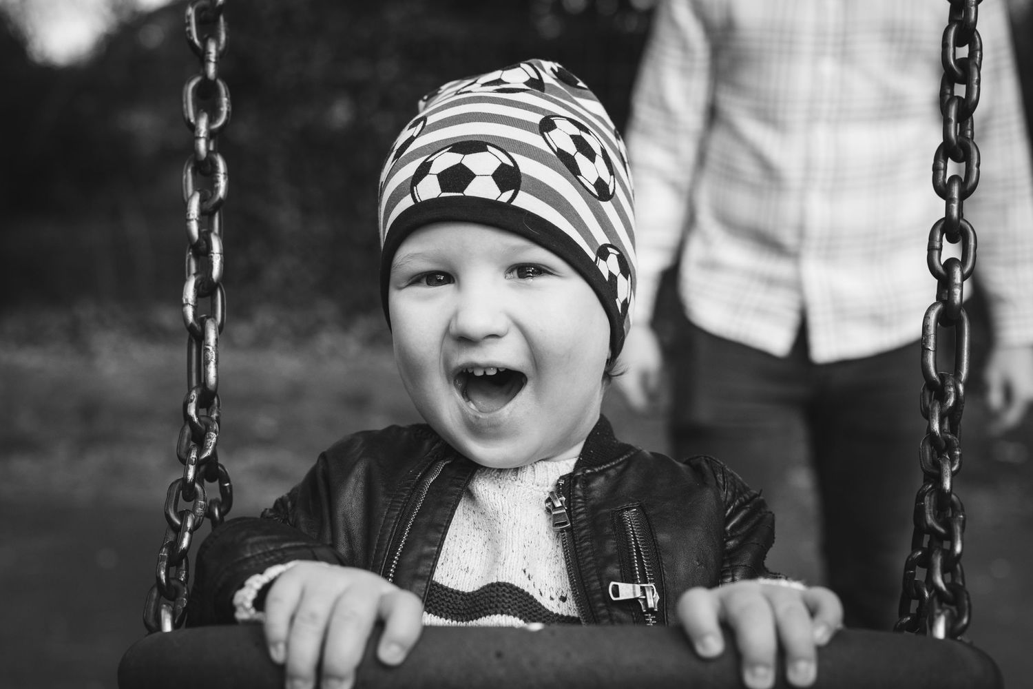 Child wearing striped hat laughing joyfully while sitting on a swing.