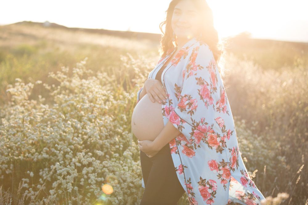 Backlit maternity photo of pregnant woman in floral dress during golden hour.