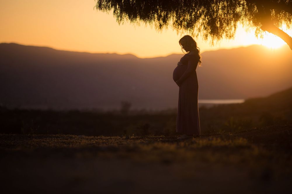 Silhouette of pregnant woman standing against mountain sunset backdrop.