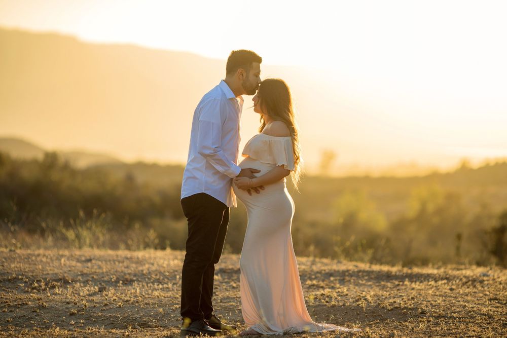 Silhouetted couple shares intimate moment during sunset maternity photoshoot.