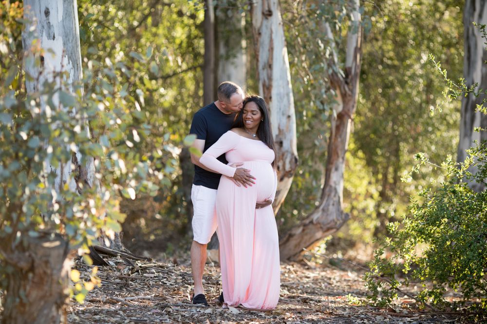 Expecting couple embraces among eucalyptus trees in outdoor maternity photo.
