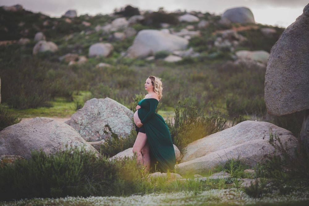 A woman in an emerald dress poses elegantly among large boulders in nature.