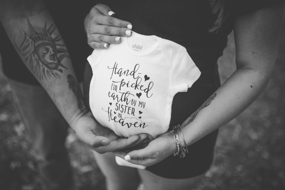 Black and white photo of hands holding a baby onesie with text.