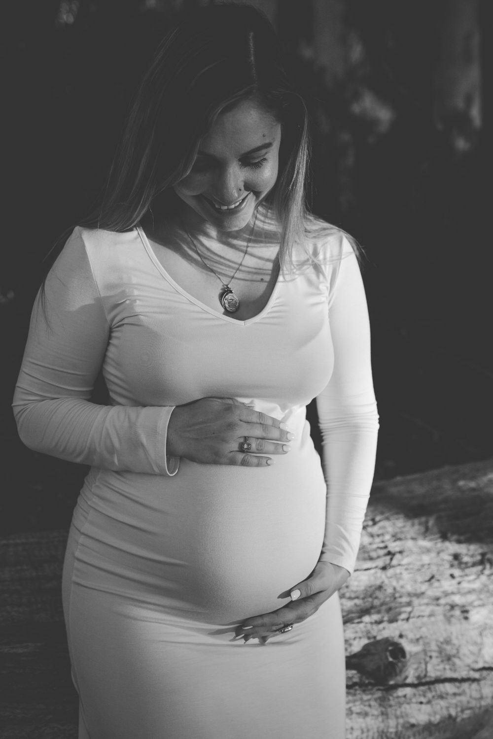 Black and white portrait of pregnant woman in white dress holding her belly.