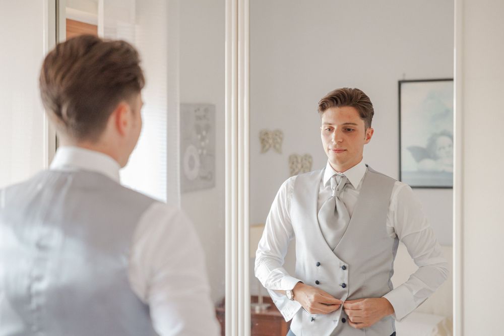A person adjusts their formal attire while getting ready in a bright room.