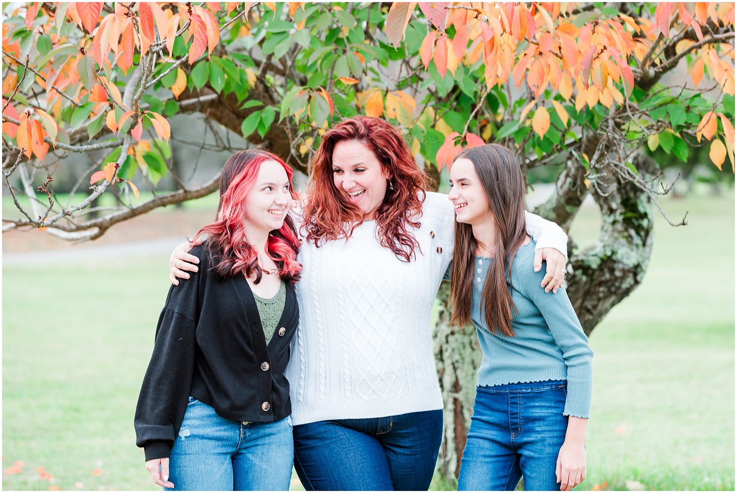 Three people share laughter while posing together against a backdrop of autumn foliage.