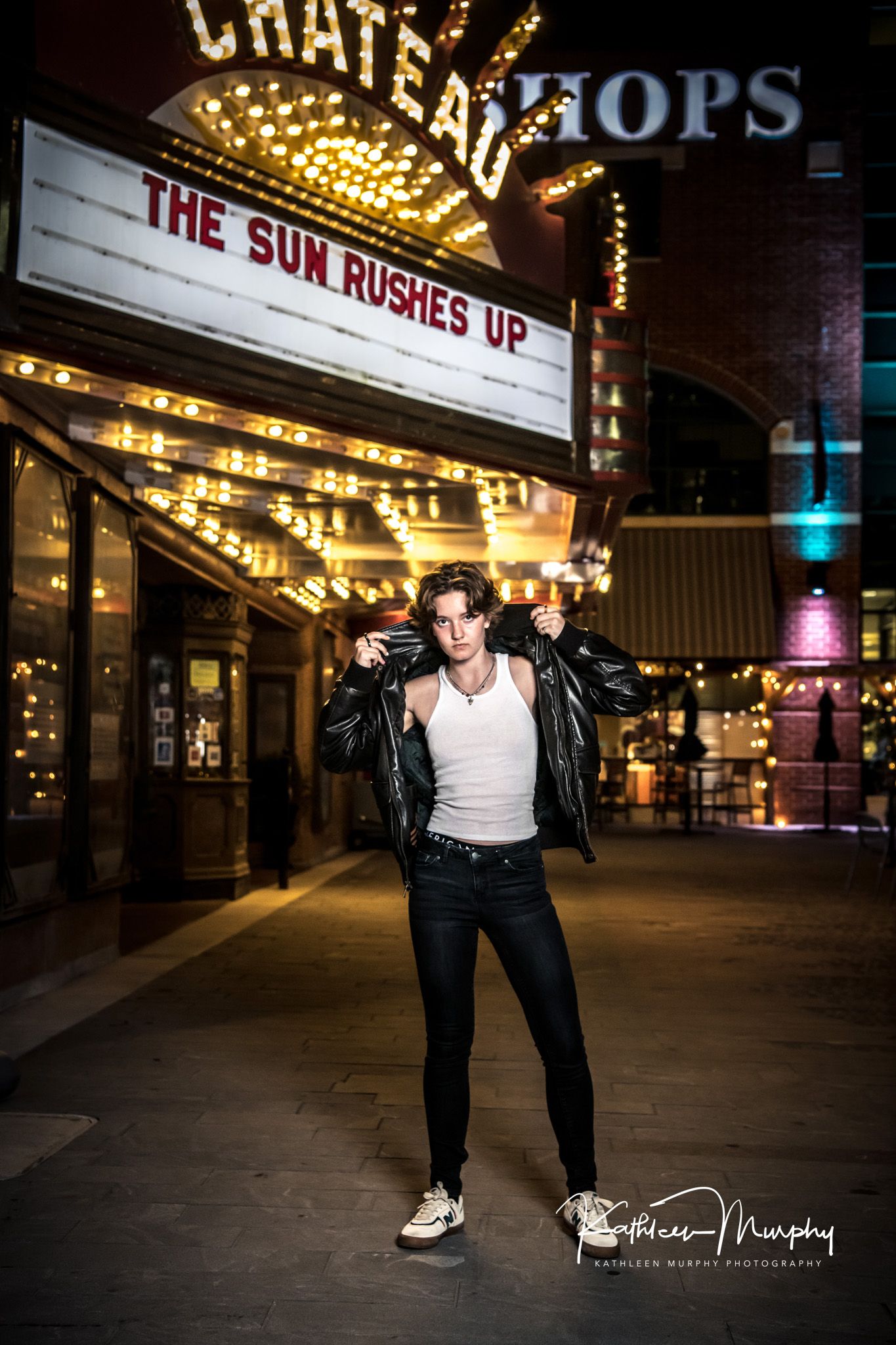 Dramatic nighttime portrait under vintage theater marquee lights reading 'The Sun Rushes Up' at Chateau theater.
