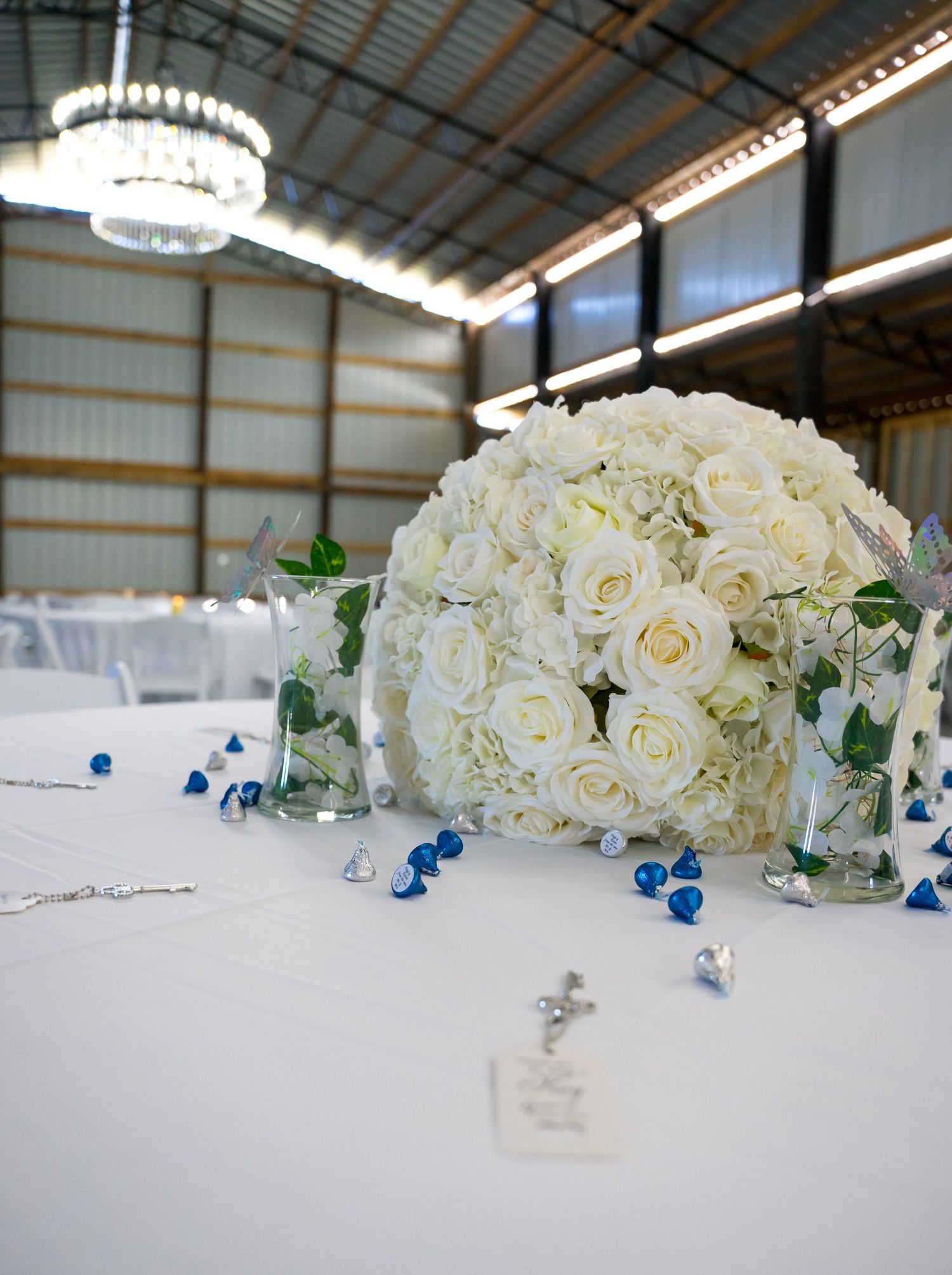 White rose floral arrangements with blue accents displayed on reception tables.